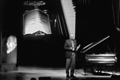 Ton-Film: Jürgen Hocker demonstriert vor einem Bild Conlon Nancarrows (links) und mit Hilfe einer Video-Kamera das Funktionieren eines Player Pianos.